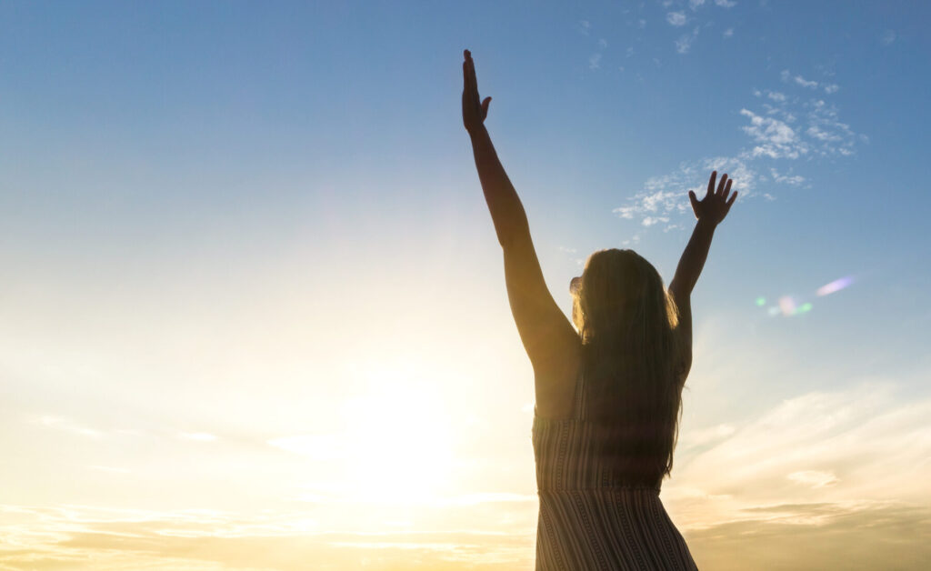 Brave happy young woman raising hands up in the air and open arms to sky. Enjoying life. Sunny healthy lifestyle concept in sunset.